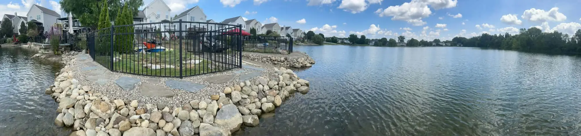 Wide panoramic view of completed shoreline boulder and fence landscaping