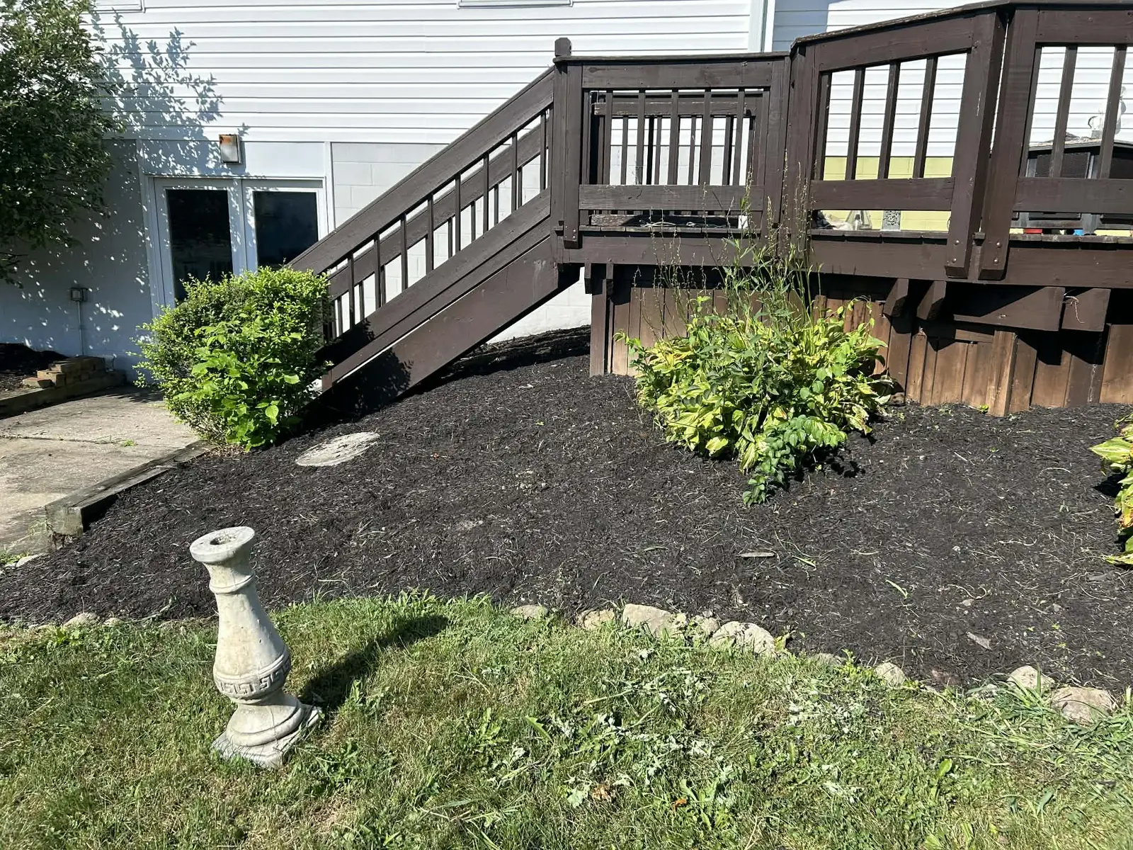 Fresh dark mulch installed around shrubs beneath a residential deck